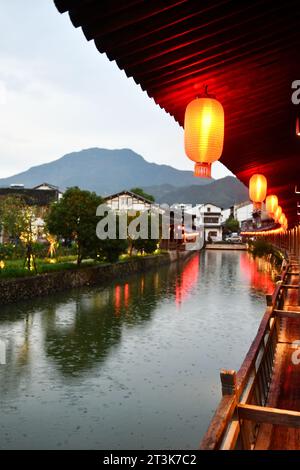 Nachtfoto eines Korridors im traditionellen chinesischen Stil, mit traditionellen chinesischen Laternen, die unter dem Traufe hängen und eine Reflexion im Fluss bilden Stockfoto