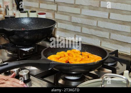 Hälften frischer Aprikosen werden in Karamellsirup in einer Pfanne auf einem Gasherd gebraten. Stockfoto