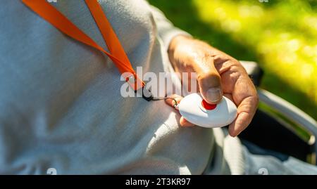 Ältere Person, die im Rollstuhl draußen den Notausschalter in der Hand drückt. Bild des Konzepts des Notrufsystems. Stockfoto