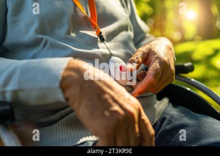 Senior Mann drückt Alarm-Taste im Rollstuhl draußen in einem Park, Nahaufnahme. Bild des Konzepts des Notrufsystems. Stockfoto