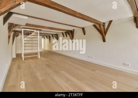 Ein leerer Raum mit Holzfußboden und freiliegenden Balken an der Decke darüber ist eine Treppe, die zum zweiten Stock führt Stockfoto