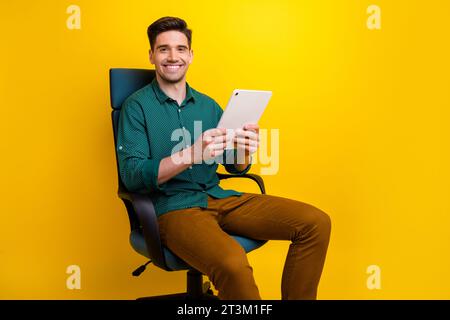 Foto des attraktiven stilvollen Mannes sitzender Sessel, der moderne Gadget ipad hält, Lesezugriff Nachrichten isoliert auf gelbem farbigen Hintergrund Stockfoto