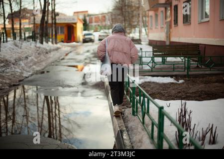 Mädchen geht im Winter die Straße entlang. Frau im Winter in der Stadt. Schlechte Straße im Hof in Russland. Der Student kehrt nach Hause zurück. Stockfoto