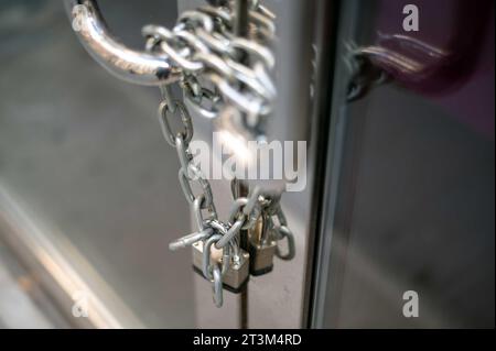 Kette und Vorhängeschloss an geschlossener Business-Glastür mit Metallgriffen Stockfoto