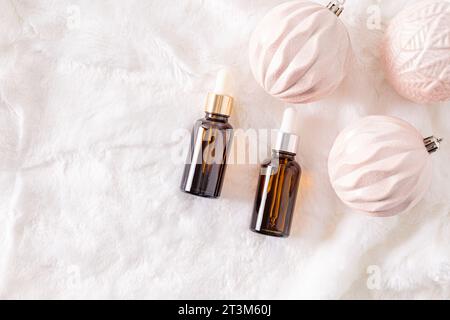 Zwei Kosmetikflaschen mit Tropfer mit natürlichem Selbstpflegeprodukt auf weißem Pelzhintergrund mit eleganten weihnachtskugeln. Eine Kopie des Bereichs. Stockfoto