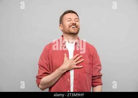 Glücklicher positiver, fröhlicher Mann, der aufrichtig lacht, mit geschlossenen Augen isoliert auf grauem Hintergrund. Stockfoto