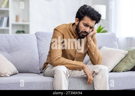 Trauriger deprimierter Mann, der zu Hause auf dem Sofa im Wohnzimmer sitzt, hoffnungslos einsam. Stockfoto