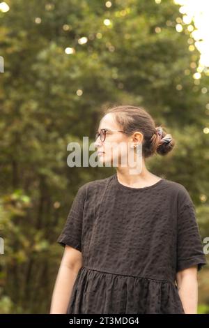 solomädchen in schwarzem Kleid und Brille, die an einigen Büschen in Osmotherly, North Yorkshire, England, Großbritannien steht Stockfoto