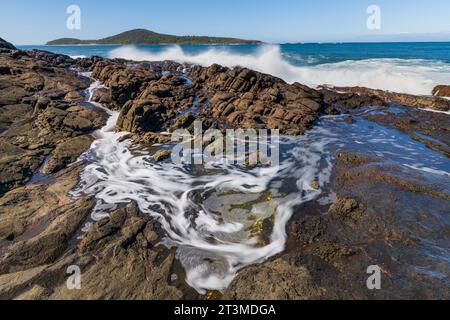 Raues Surfen über eine zerklüftete Küste und wirbeln in Felsenbecken in Fingal Bay in New South Wales, Australien Stockfoto