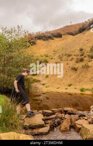 solomädchen in schwarzem Kleid an einem Moorbach unter einer Klippe in Osmotherly, North Yorkshire, England, Großbritannien Stockfoto