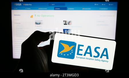 Person, die ein Mobiltelefon mit dem Logo der Agentur der Europäischen Union für Flugsicherheit (EASA) vor der Webseite hält. Schwerpunkt auf dem Display des Telefons. Stockfoto