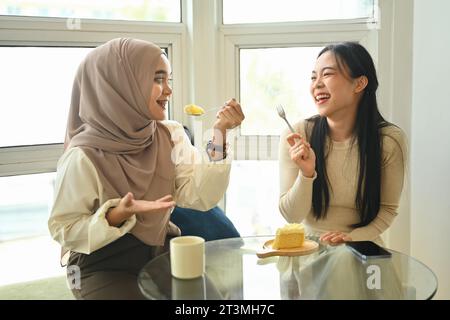 Zwei glückliche, multirassische Mädchen genießen Kuchen und trinken Kaffee in einem Café Stockfoto