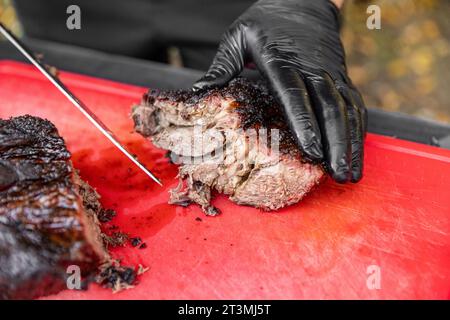 Koch in schwarzen Kochhandschuhen mit Messer zum Schneiden von geräuchertem Schweinefleisch Stockfoto