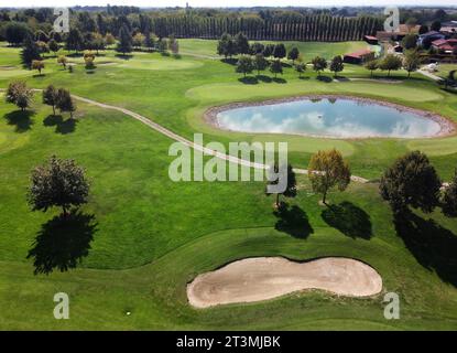 Drohnenblick auf grünen, grasbewachsenen Golfplatz mit kleinem Teichwasser, das blauen, bewölkten Himmel reflektiert, sandigem Gelände, Wanderweg über Gras und Bäume mit b Stockfoto