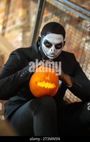 Mann in weißer Make-up-Maske lehnt sich an Kürbis Stockfoto