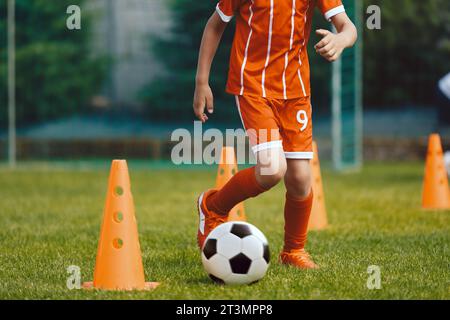 Kinder üben Dribbeln auf dem Fußballfeld. Junge, der Fußball im Slalomtraining zwischen Trainingskegeln läuft Stockfoto