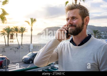 Mann am Smartphone - junger Geschäftsmann, der mit dem Smartphone spricht. Lässiger, städtischer Geschäftsmann mit Handy lächelnd, glücklich zu Fuß. Stockfoto