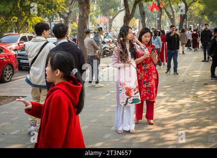Eine vietnamesische Mutter mit ihrer Tochter, die eine Pfirsichblüte hält und beide in traditionellem ao dai in Tet, oder Mondneujahr, im Zentrum von Hanoi, Vietnam, gekleidet ist Stockfoto
