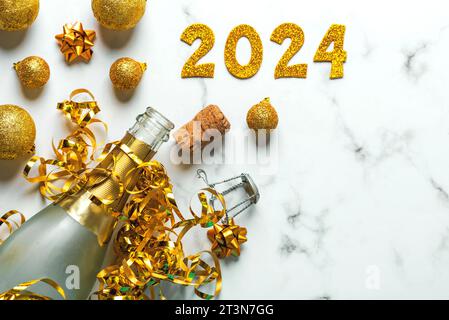 Frohes neues Jahr 2024. Flasche Champagner mit weihnachtskugeln und goldenen Zahlen mit der Nummer 2024 auf Marmortisch. Silvesterfeier Co Stockfoto