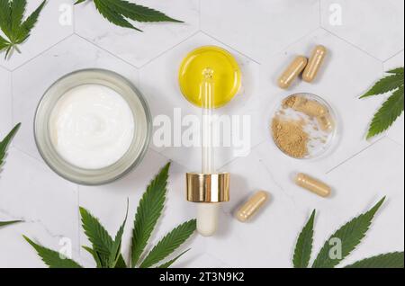Kosmetikglas, Pipette mit CBD-Öl und Kapseln mit Hanfpulver in der Nähe von grünen Cannabisblättern auf einem Marmortisch. Bio-Hautpflege und Gesundheitsauto Stockfoto