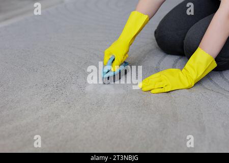 Nahaufnahme der weiblichen Hände in gelben Gummihandschuhen Teppich mit Bürste und Schaum reinigen, Kopierraum über grauem Teppich Stockfoto