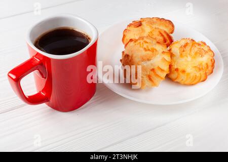 Goldene Profiteroles gefüllt mit Sahne, serviert mit einer Tasse Kaffee auf weißem Tisch. Ein köstliches Dessert für jeden Anlass. Stockfoto