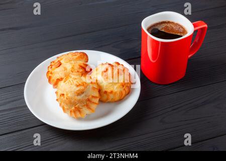 Goldene Profiteroles gefüllt mit Sahne, serviert mit einer Tasse Kaffee auf dunklem Tisch. Ein köstliches Dessert für jeden Anlass. Stockfoto