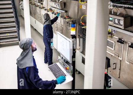 Vaterstetten, Deutschland. Oktober 2023. Zwei BMW-Mitarbeiter arbeiten im Trocknungsbereich einer Werkshalle während einer Pressebesichtigung des BMW Cell Manufacturing Competence Centre (CMCC) in Parsdorf an einem Monitor. In der Halle wird der Kupferstreifen der Anode, der mit der Batteriepaste („Slurry“) beschichtet ist, getrocknet. Quelle: Matthias Balk/dpa/Alamy Live News Stockfoto