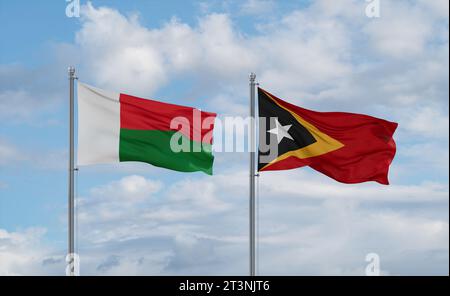 Osttimor- und Madagaskar-Flaggen winken zusammen im Wind auf blauem bewölktem Himmel, zwei Länder-Beziehungskonzept Stockfoto