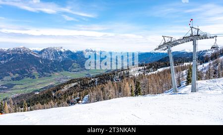 Skilift im alpinen Skigebiet. Spätwinterschnee in den Bergen und grünes Gras im Tal. Schladming, Österreich Stockfoto