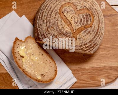 Flache Lage einer glutenfreien Sauerteigboule mit Herzform auf einer Holzbrotplatte. Stockfoto