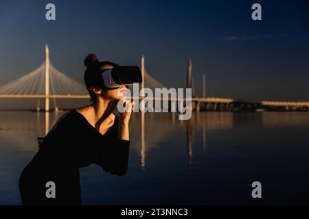 Die junge Frau verwendet eine virtuelle oder Augmented-Reality-Brille in magischer Atmosphäre von Sonnenstrahlen, weiblicher VR Stockfoto