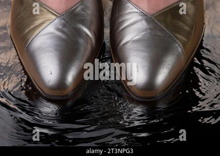 Frauenfüße in Lederschuhen mit hohem Absatz, stehend mit Zehen im flachen Wasser Stockfoto