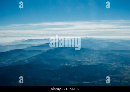 Ein atemberaubender Blick aus der Vogelperspektive auf sanfte Bergketten, die von Nebel bedeckt sind, im Kontrast zu einem ruhigen blauen Himmel voller sanfter Wolken Stockfoto