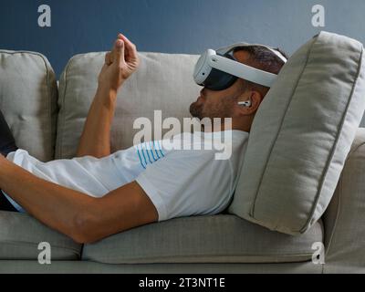 Mann, der eine Virtual Mixed-Reality-Brille verwendet, ein vr-Headset der neuen Generation für Unterhaltung trägt und auf dem Sofa liegt. Stockfoto