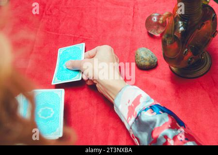 First Person Draufsicht einer nicht erkennbaren kaukasischen Frau, die blaue Tarotkarte mit roter Tischdecke auf den Tisch legt, Tarotkonzept, Kopierraum Stockfoto