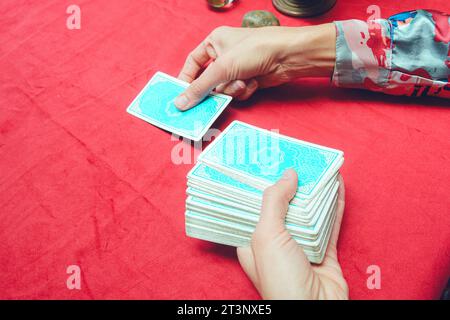 First Person Draufsicht einer nicht erkennbaren kaukasischen Frau, die blaue Tarotkarte mit roter Tischdecke auf den Tisch legt, Tarotkonzept, Kopierraum Stockfoto