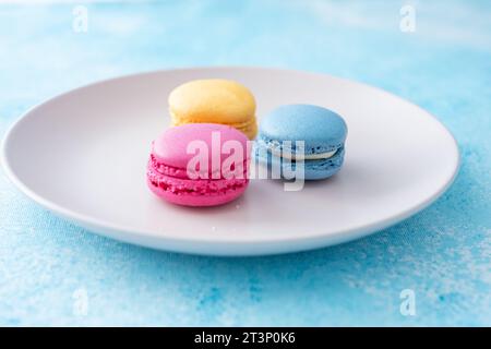 Drei verschieden farbige Macarons auf einem rosa Teller auf blauem Hintergrund Stockfoto