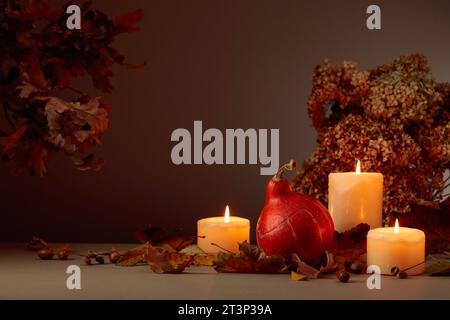Stillleben mit Kürbis, ausgetrockneten Blättern und brennenden Kerzen. Im Hintergrund getrocknete Hortensienblüten und Eichenzweige. Herbstkonzept. Stockfoto