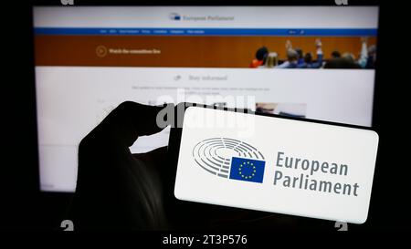 Person, die ein Mobiltelefon mit dem Logo des EU-Gesetzgebungsorgans des Europäischen Parlaments (EP) vor der Webseite hält. Schwerpunkt auf dem Display des Telefons. Stockfoto