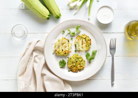 Zucchini-Kekse. Vegetarische Gemüsezucchini-Pfannkuchen auf Teller auf hellem hölzernem Hintergrund. Draufsicht, flach Stockfoto