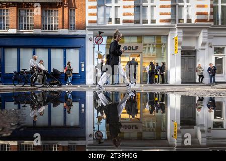 London, 26. Oktober 2023. Wetter in Großbritannien – Menschen reflektierten sich in einer Pfütze am Straßenrand in der Beak Street in der Nähe der Carnaby Street. Die Prognose ist für trockenere Bedingungen vor einem möglicherweise nassen Wochenende. Quelle: Stephen Chung / Alamy Live News Stockfoto