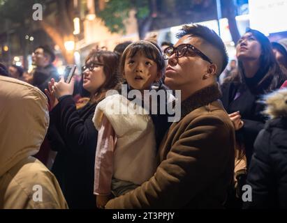 Ein vietnamesischer Vater hält seine kleine Tochter in einer Menschenmenge fest, um ein Feuerwerk in Tet oder Lunar Silvester in Hanoi, Vietnam, zu sehen. Stockfoto