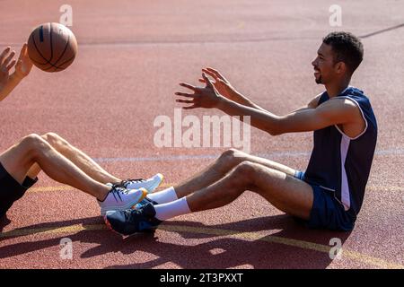 Männer, die auf dem Basketballfeld sitzen, nachdem sie das Spiel gespielt haben, werfen sich gegenseitig Ball zu. Stockfoto