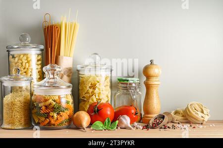 Auswahl an trockenen italienischen Nudeln in Glasbehältern und Gewürzen auf Holztisch. Stockfoto