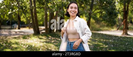 Das stilvolle asiatische Mädchen geht im Park spazieren, lacht und genießt das Sommerwetter. Menschen- und Lifestyle-Konzept Stockfoto