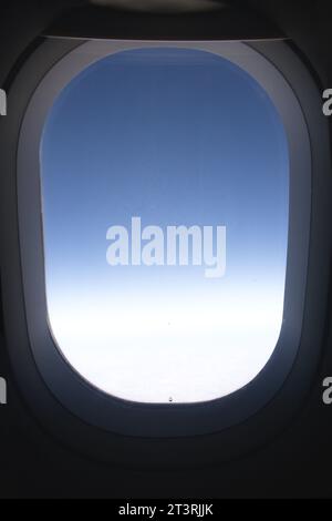Nahaufnahme eines Fensters aus dem Inneren eines Flugzeugs, das den blauen Verlauf der oberen Atmosphäre zeigt Stockfoto