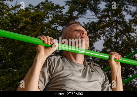 Der Mann zieht sich in eine grüne Sportbar. Fitness am frühen Morgen. Sein Gesicht wird von ersten Sonnenstrahlen beleuchtet. Stockfoto