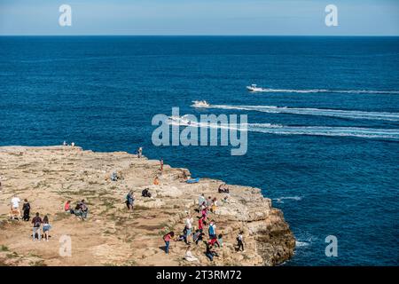 Menschen, die das sonnige Wetter auf dem Felsvorsprung gegenüber dem Strand Cala Ponte in Polignano a Mare, Italien, genießen, Stockfoto