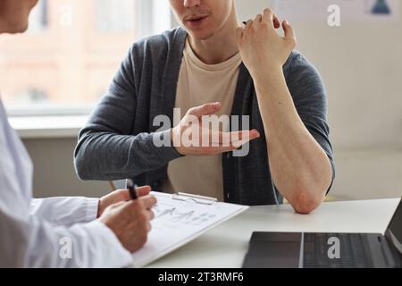 Nahaufnahme eines Mannes, der auf Hautausschlag an den Unterarmen zeigt, während er sich mit dem Dermatologen in der Klinik berät, Kopierraum Stockfoto
